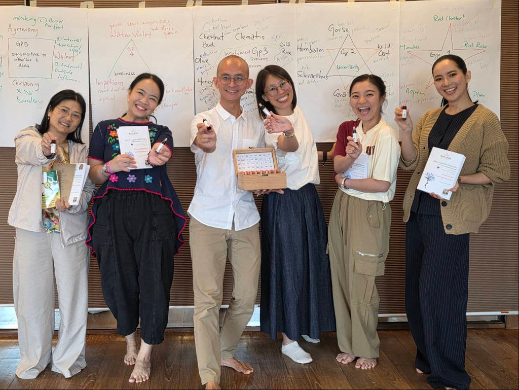 Six people standing together in front of a wall with large whiteboards covered in handwritten notes, each holding a small product and a certificate. The setting appears to be an indoor workshop or presentation space.